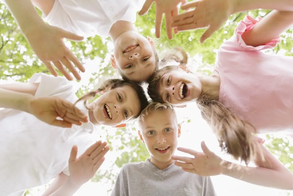 Quatre enfants heureux sous les arbres, sourires communicatifs.